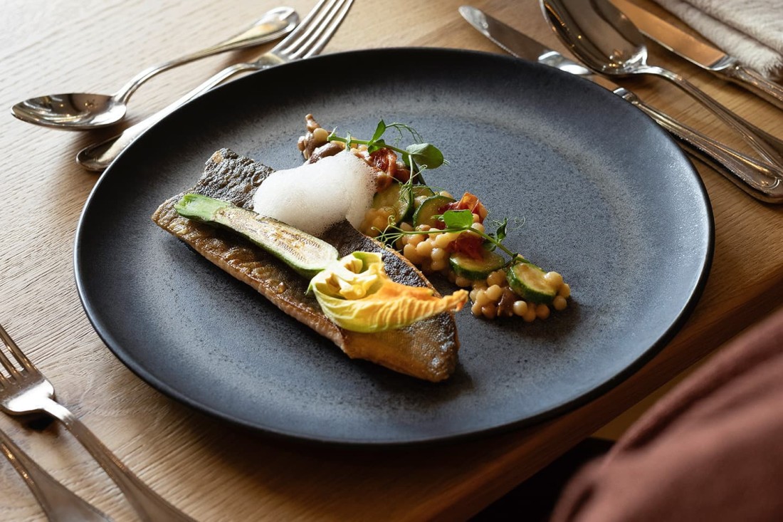 Elegantes Fischgericht mit Zucchini und Garnitur auf einem schwarzen Teller