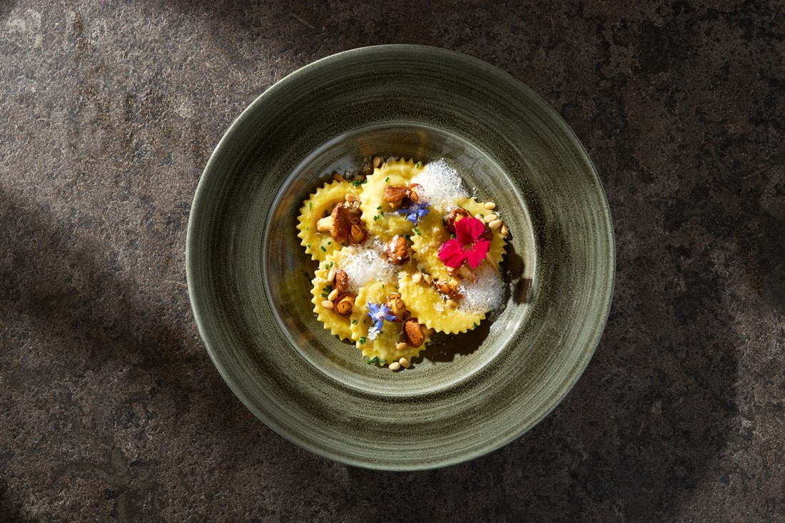Ein Teller mit dekorierten Ravioli, garniert mit N&uuml;ssen, Bl&uuml;ten und Schaum im Restaurant seven's kitchen