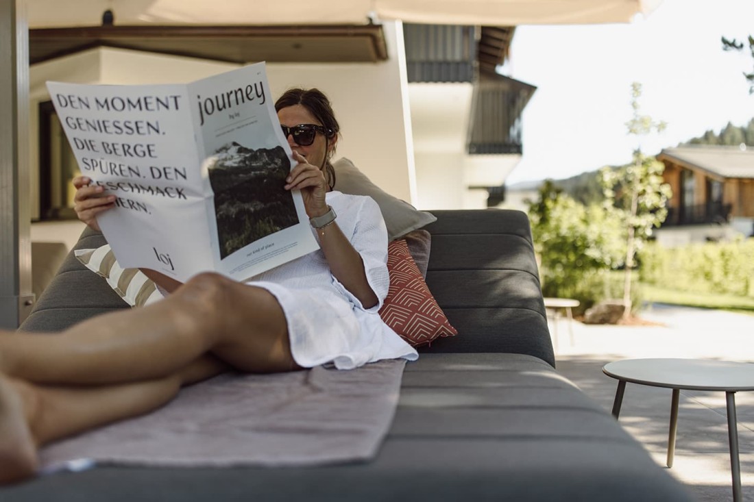 Eine Frau liest drau&szlig;en das Hotel-Magazin vom loj auf einem grauen Sofa