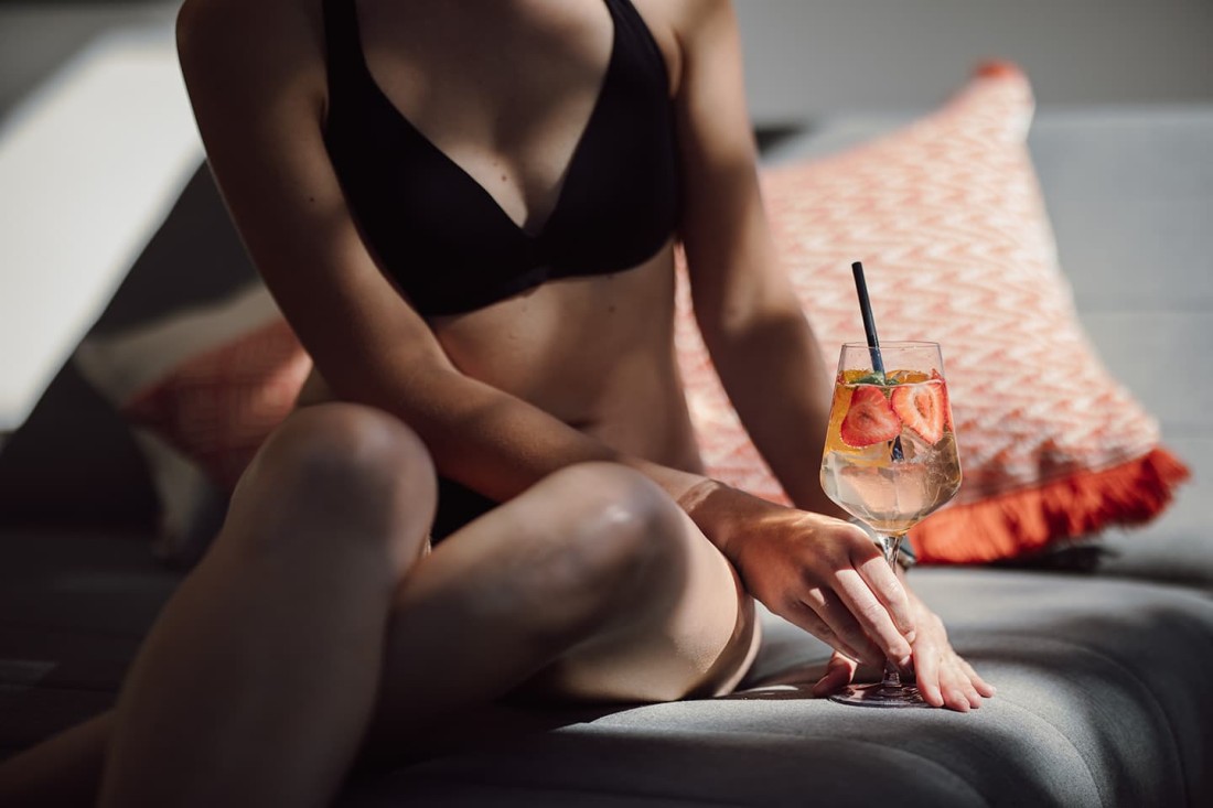 Person im Bikini h&auml;lt ein Getr&auml;nk mit Erdbeeren auf einem Sofa