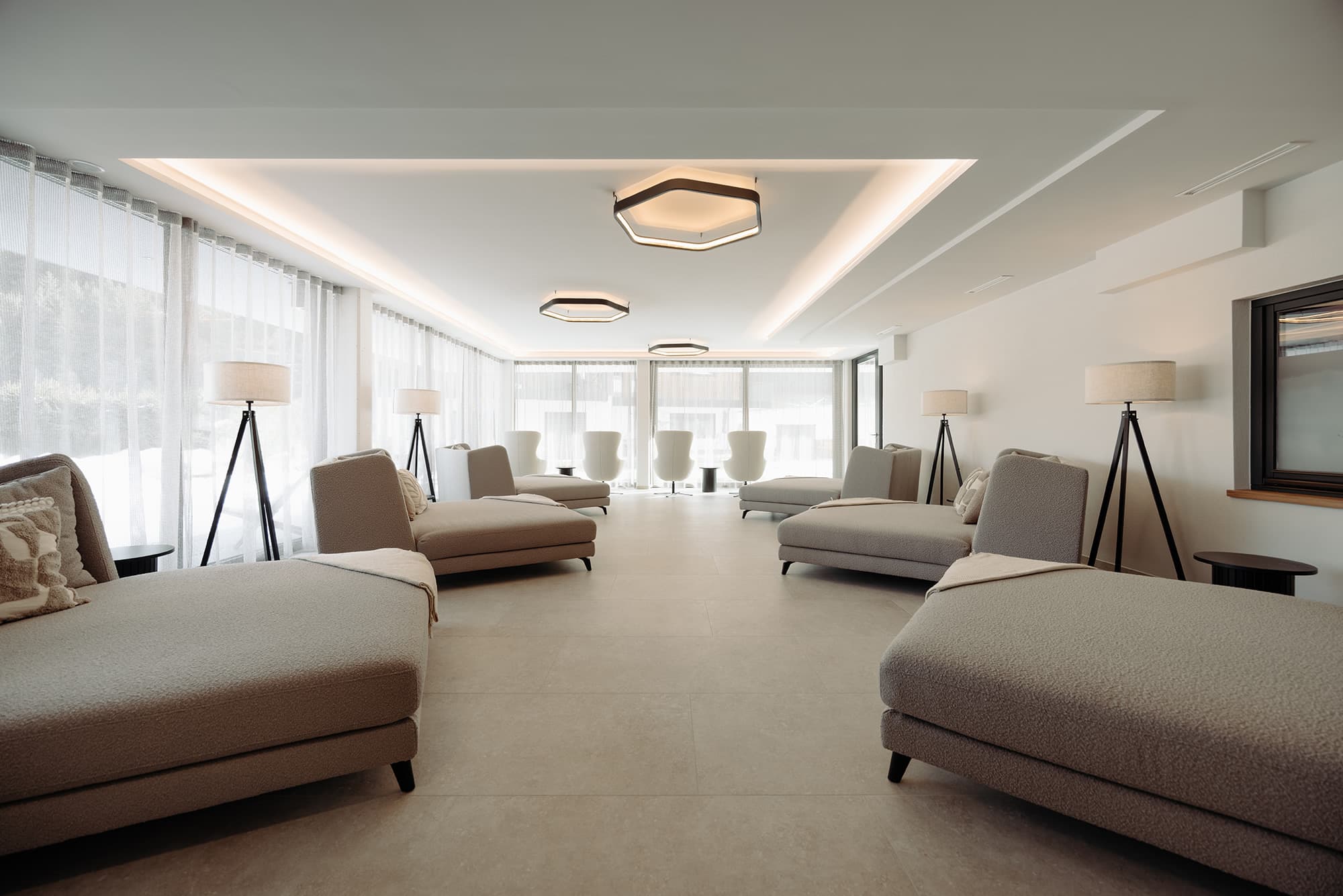 Moderner Ruheraum mit Lounge-Bereich mit grauen Sofas, Stehlampen und gro&szlig;en Fensterfronten im Wellnesshotel loj in Flachau