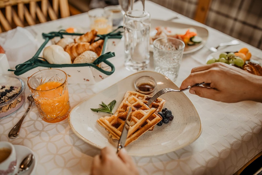 Eine Person schneidet Waffeln auf einem Tisch mit verschiedenen Fr&uuml;hst&uuml;cksgerichten