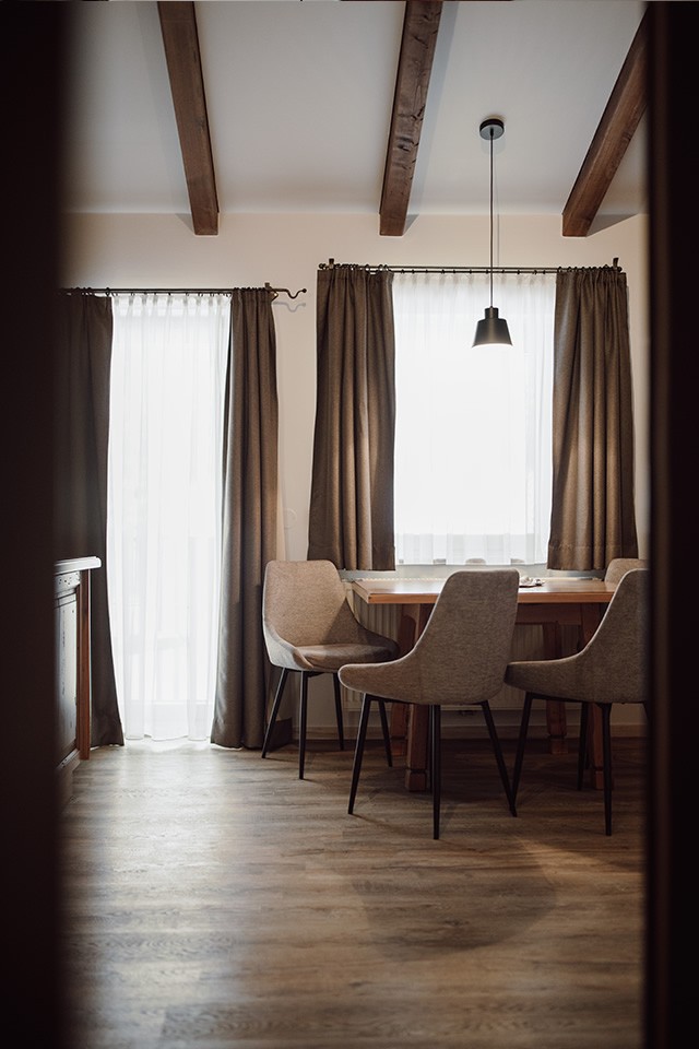 Esszimmer mit Holztisch, vier St&uuml;hlen und braunen Vorh&auml;ngen an den Fenstern